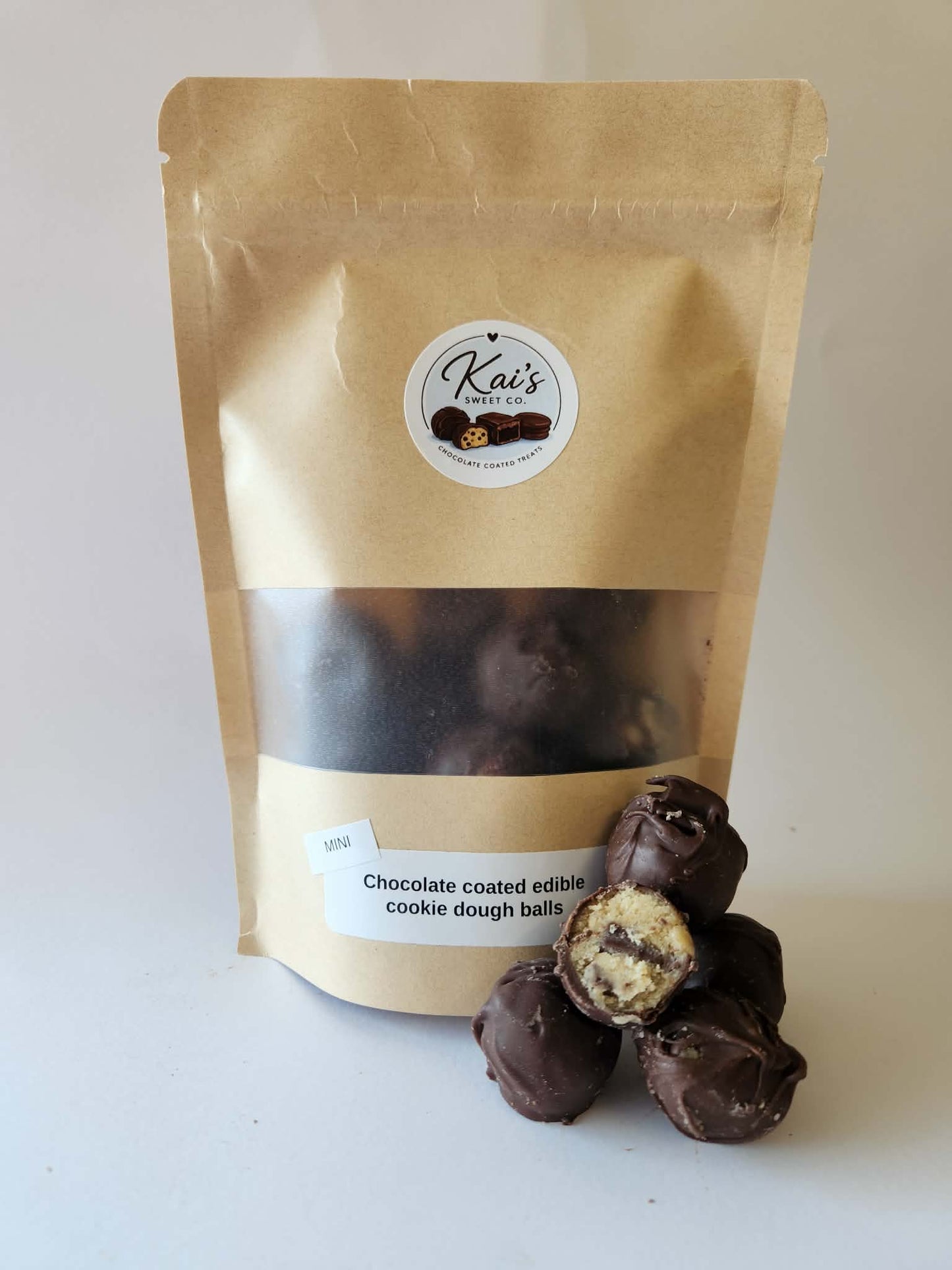 Kai's Sweet Co Mini Chocolate Coated Edible Cookie Dough Balls in branded kraft bag with window, one cut open showing cookie dough filling