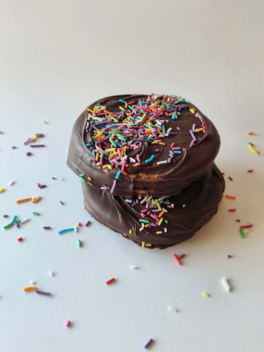 Kai's Sweet Co The Angelique Roundabout two stacked, milk chocolate coated with rainbow sprinkles on white background