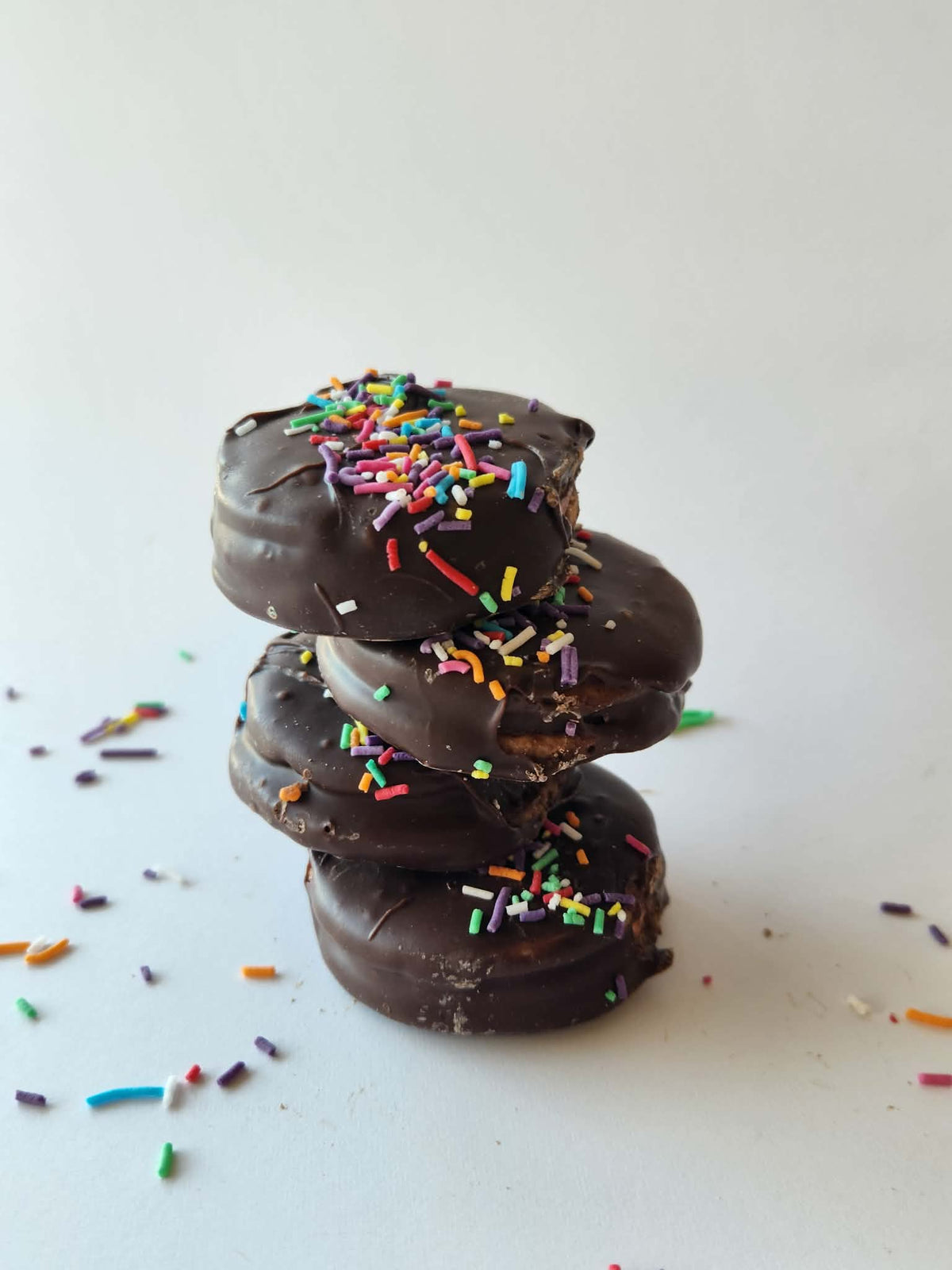 Kai's Sweet Co The Angelique Mini Roundabouts stacked three high, chocolate coated with rainbow sprinkles