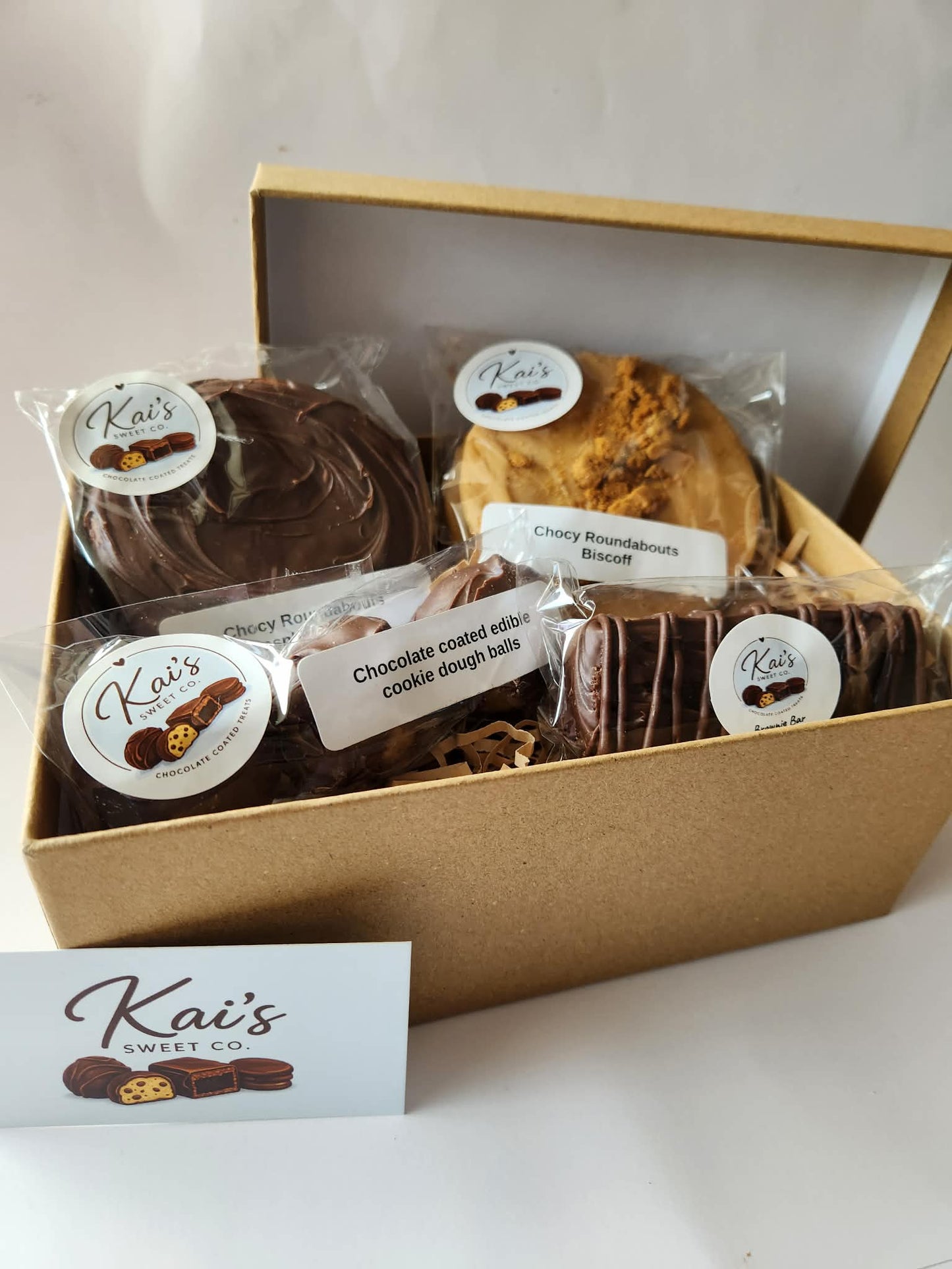 Kai's Sweet Co Small Gift Box open showing Raspberry Jam and Biscoff chocolate roundabouts, cookie dough balls and a chocolate fudge brownie bar in kraft box with shredded paper